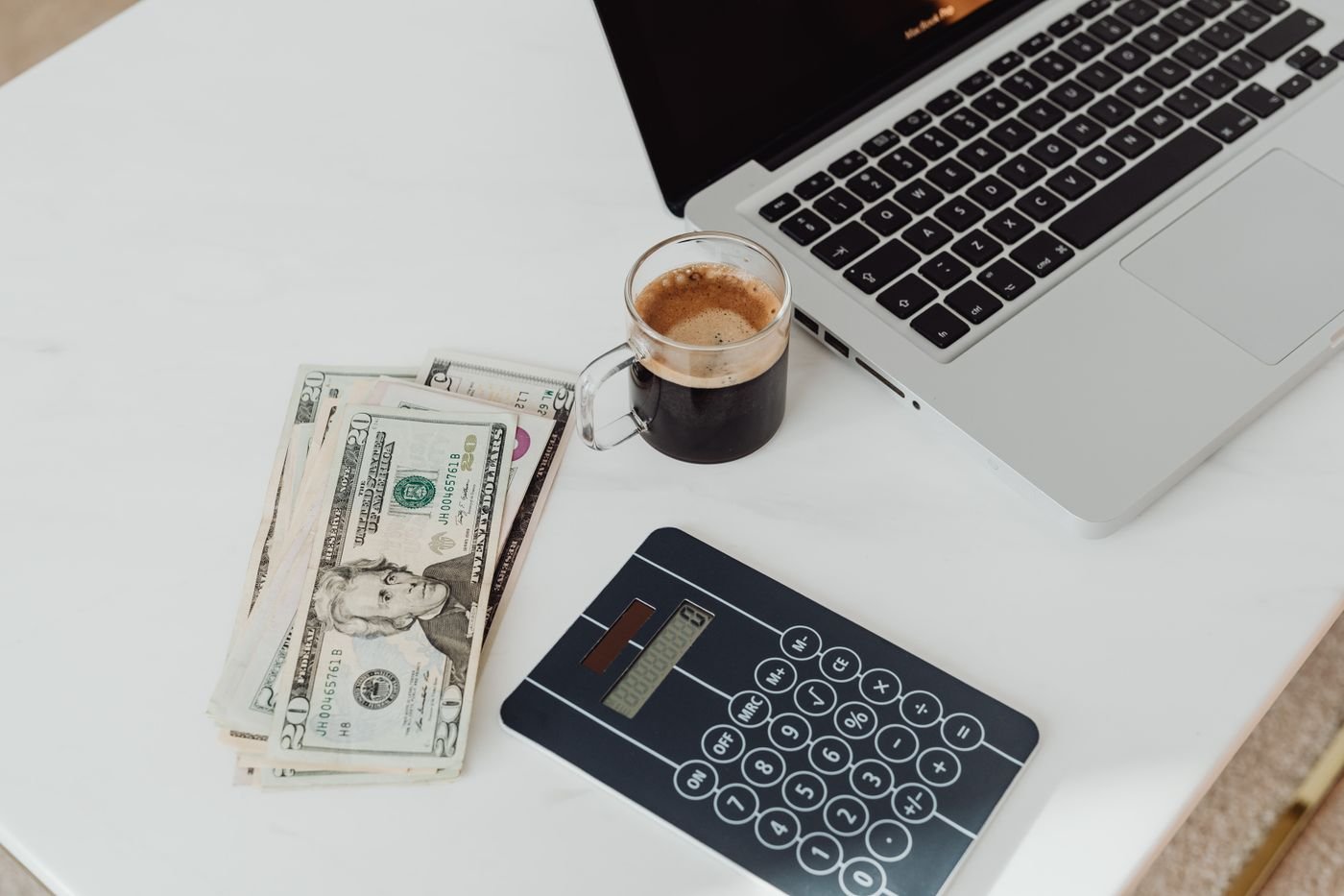Calculator, money and laptop on a desk — illustrative photograph